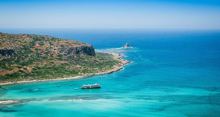 Mar turquesa con un barco acercándose a una costa bordeada de acantilados en Creta.