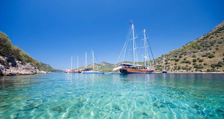 Crystal-clear lagoon with anchored yachts framed by green hills under a vivid blue sky.