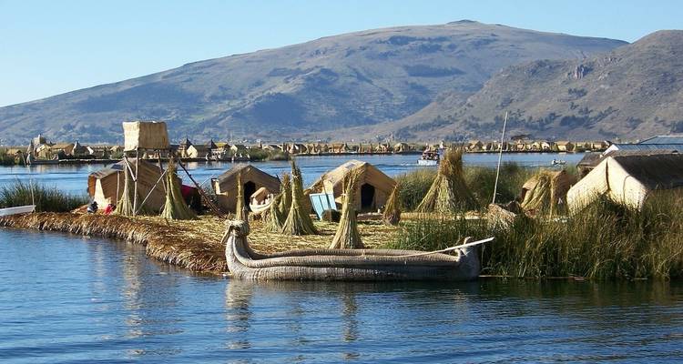 Lago con barcas de totora y pequeñas chozas al fondo.