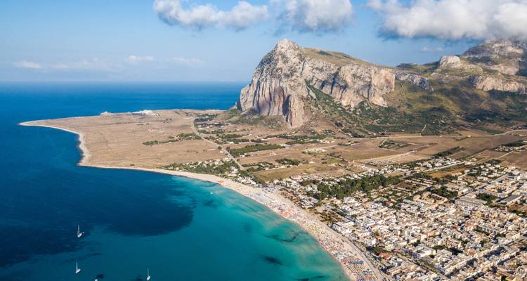 Vue aérienne d'une baie turquoise, d'une large plage de sable et d'une falaise spectaculaire près d'une ville côtière sicilienne.