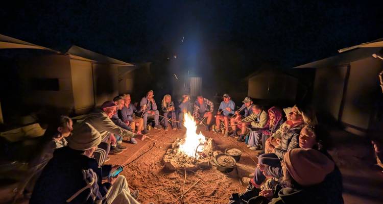 Groupe de voyageurs réunis autour d'un feu de camp brillant sur un site de camping désertique sous le ciel nocturne