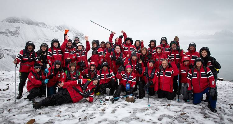 Grand groupe d'expédition posant en vestes rouges sur une crête enneigée avec des pics brumeux en arrière-plan
