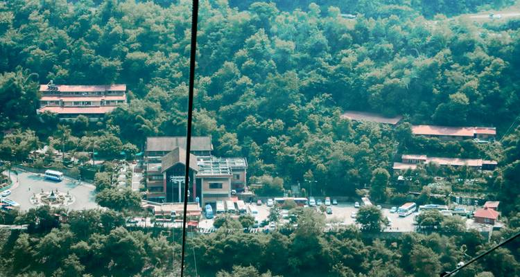 Vista aérea del complejo turístico en una ladera boscosa y estacionamiento vistos a través de los cables del teleférico.