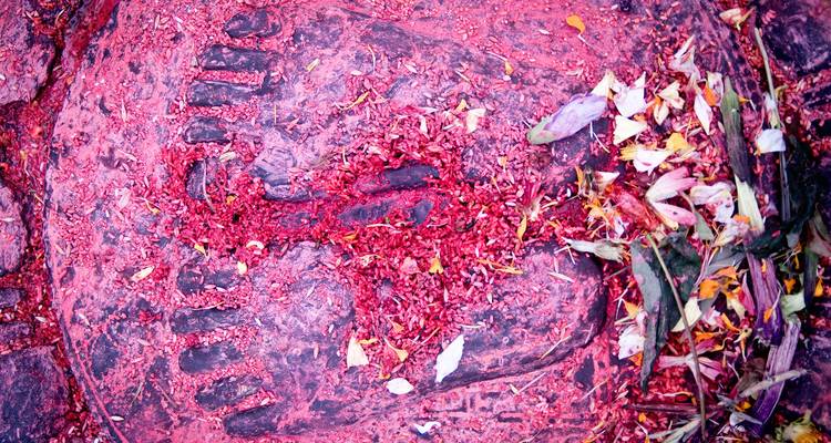Primer plano de una superficie de piedra teñida de rojo con granos de arroz y hojas esparcidas de una ofrenda religiosa.