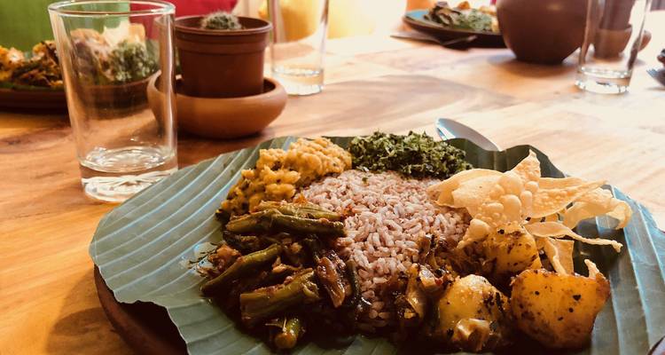 Repas de riz et curry sri-lankais servi sur une feuille de bananier à une table en bois rustique.