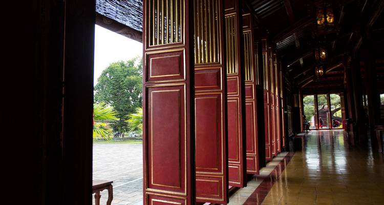 Fila de altas puertas lacadas en rojo dentro de un corredor de ciudadela vietnamita tradicional que se abre a una vista del patio