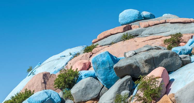 Cluster of pastel-painted boulders set against a cloudless sky with small shrubs.