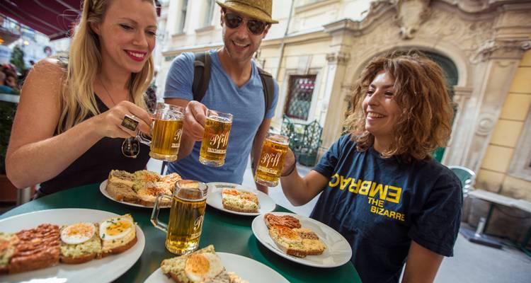 Groupe d'amis trinquant avec des chopes de bière sur des collations locales à une terrasse de café extérieure.