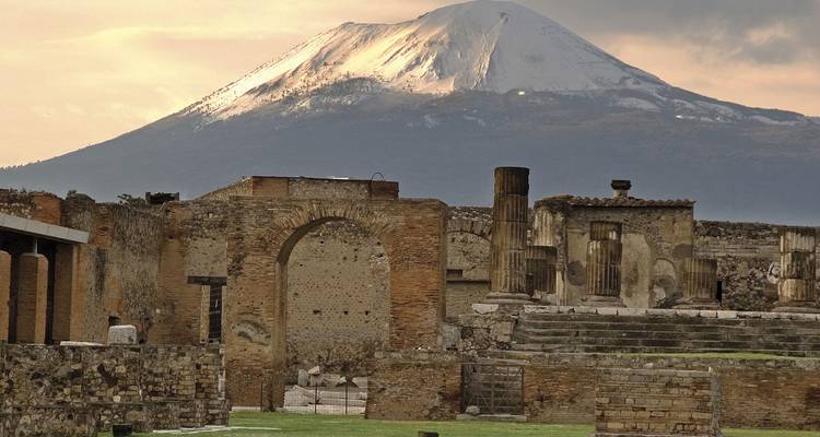 Les ruines anciennes de Pompéi avec le majestueux Mont Vésuve aux pics enneigés s'élevant au loin sous une lumière de soirée chaleureuse.