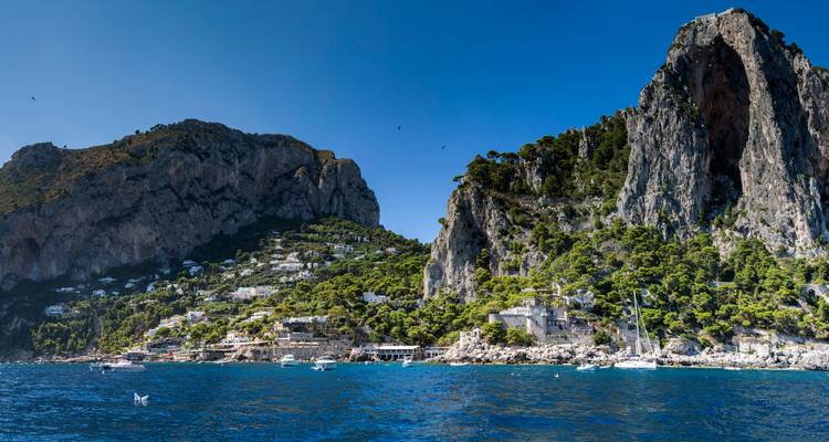 Les falaises calcaires spectaculaires et les pentes verdoyantes de l'île de Capri s'élevant des eaux bleu vif parsemées de bateaux.