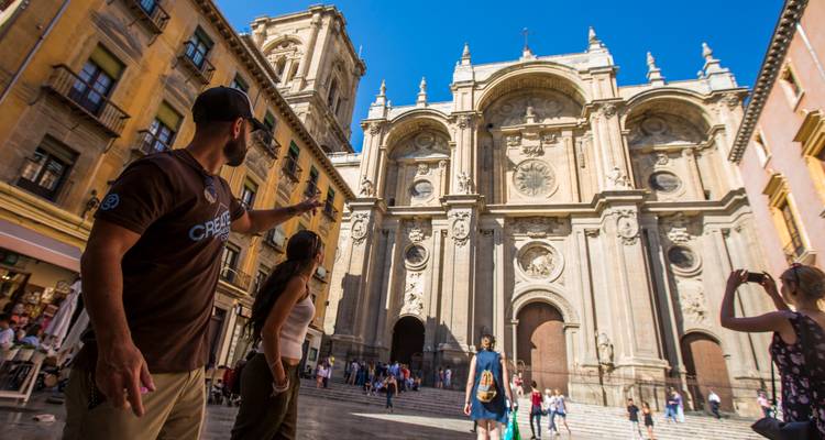 Visitantes señalando hacia la ornada fachada del Renacimiento de la Catedral de Granada en una animada plaza.