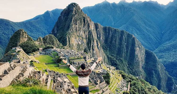 Viajero con los brazos levantados contempla la antigua ciudad de piedra de Machu Picchu rodeada de exuberantes picos