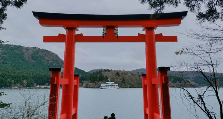 Torii rouge avec lac et ferry en arrière-plan.
