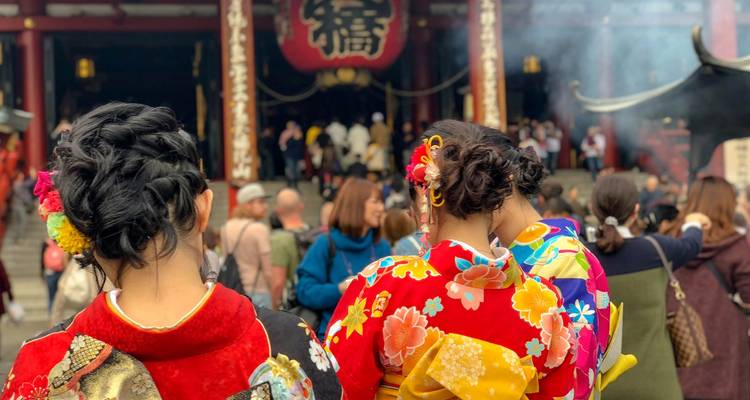 Des femmes vêtues de kimonos colorés se tiennent dos à la caméra dans une cour de temple bondée remplie de fumée d'encens.