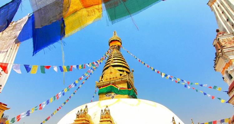 Colorful prayer flags frame the golden spire of Swayambhunath Stupa against a vivid blue sky.