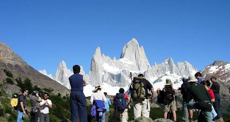 Große Gruppe von Wanderern pausiert auf einem Pfad, während die gezackten, schneebedeckten Spitzen des Mount Fitz Roy vor ihnen aufragen.