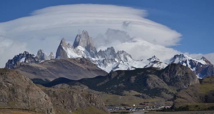 Der ikonische Berg Fitz Roy, umrahmt von einer dramatischen Linsenwolke oberhalb von sanften Hügeln und einer kleinen Stadt darunter