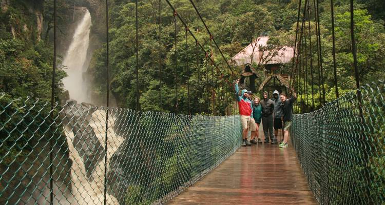 Grupo de personas en un puente colgante con una cascada de fondo.
