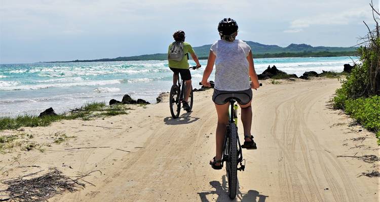 Dos ciclistas andando por un sendero de playa arenosa.