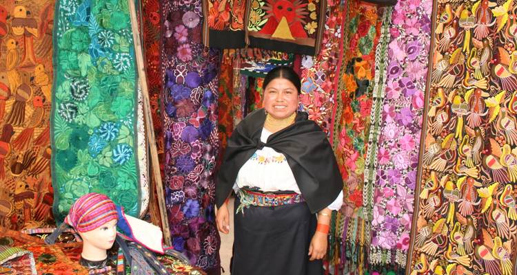 Verkäufer posiert vor bunten Schals auf einem Markt.