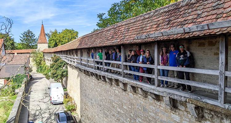 Groupe de touristes debout sur le mur d'enceinte médiéval couvert de Rothenburg surplombant les ruelles pavées et les toits.