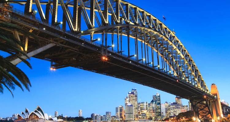 Le pont du port de Sydney s'arque au-dessus de la ligne d'horizon scintillante de la ville au crépuscule, avec l'Opéra visible en dessous.