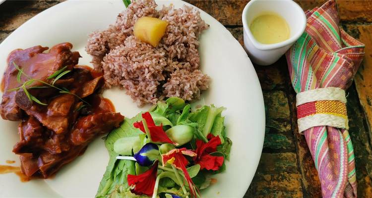 Colorful Filipino meal with rice, saucy meat, fresh salad and dressing served on rustic table.