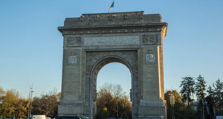 Le monument de l'Arcul de Triumf à Bucarest se dressant sous un ciel bleu dégagé avec le trafic en dessous.