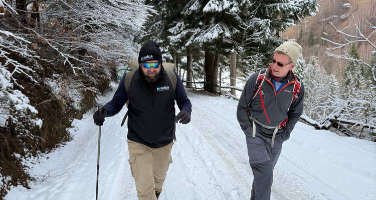 Dos excursionistas caminan por un camino forestal nevado en los Montes Cárpatos, charlando alegremente.