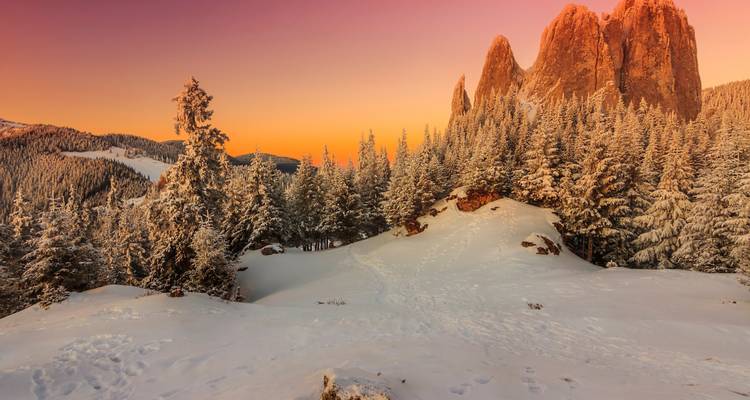 Spectaculaire zonsondergang in een besneeuwd berglandschap met levendige luchtkleuren.