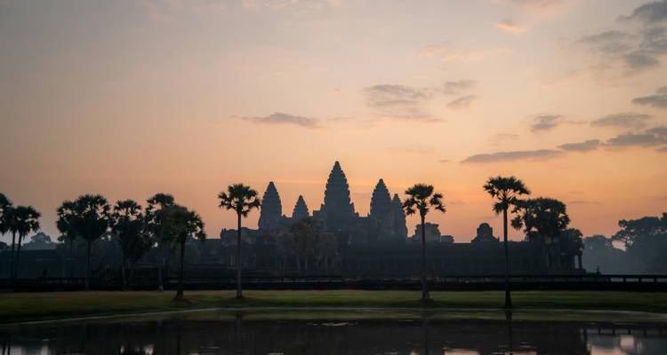 Silhouet van Angkor Wat tempels weerspiegeld in een vijver bij zonsopgang met pastelkleurige lucht.