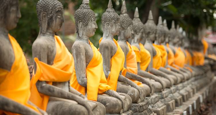 Reihe von steinernen Buddha-Statuen in orangefarbene Gewänder gehüllt in einem alten Tempel.