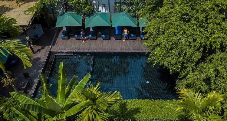 Luftaufnahme eines Boutique-Hotels mit Pool, umgeben von üppigen tropischen Bäumen und grünen Sonnenschirmen.