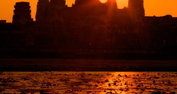 Coucher de soleil sur la silhouette d'un temple avec de l'eau et des reflets.