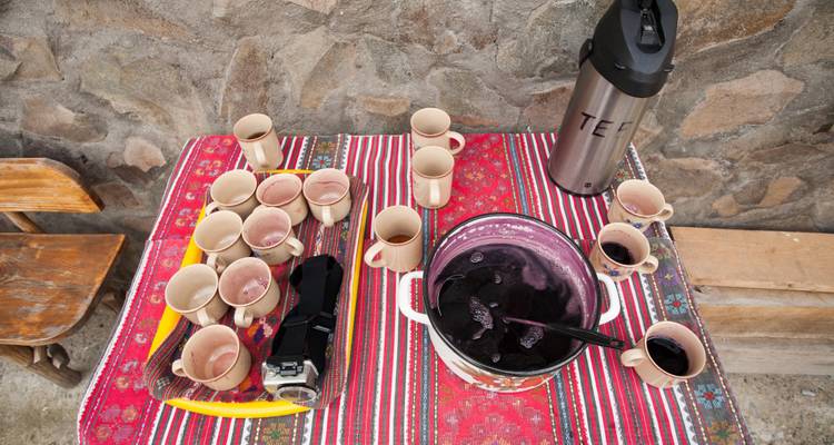 A table with cups of tea and a pot on a colorful cloth.
