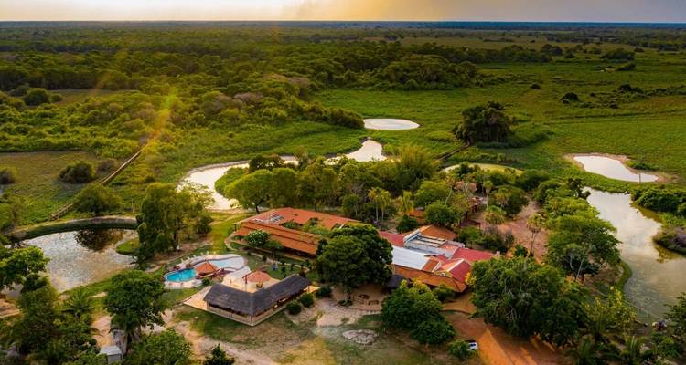 Luftaufnahme bei Sonnenuntergang einer Öko-Lodge-Anlage, umgeben von Feuchtgebieten und Wald im Pantanal.