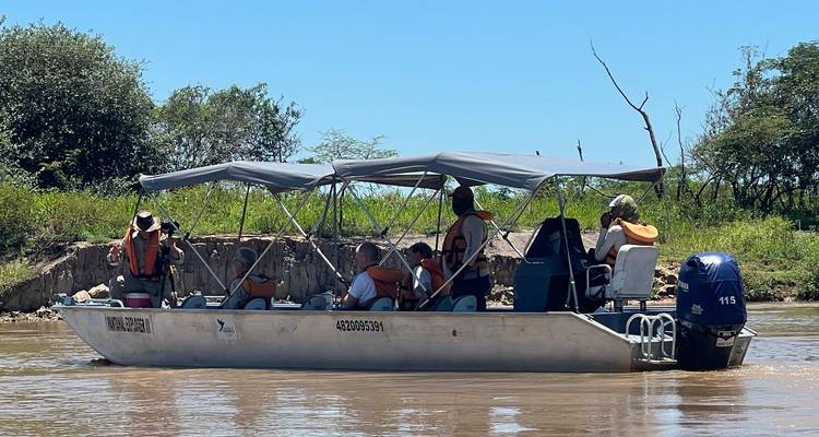 Metallisches Flachboot mit Verdeck, das Vogelbeobachter auf einem schlammigen Fluss bei starker Sonneneinstrahlung befördert.