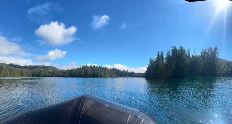 Aussicht von einem aufblasbaren Boot auf einen blauen See, der von immergrünem Wald unter klarem Himmel umgeben ist.
