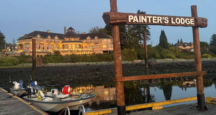 Anlegestelle und Boote mit Schild der Painter's Lodge und historisches Waterfront-Hotel bei Dämmerung beleuchtet.