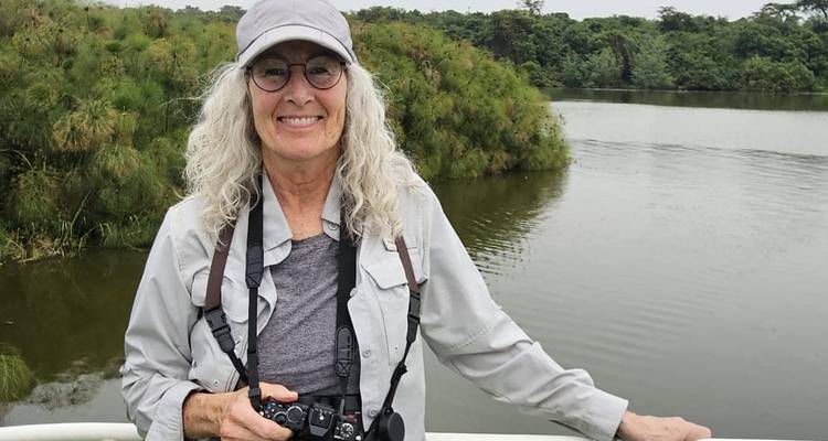 Mujer con cámara de pie en la cubierta del bote mirando hacia un tranquilo lago rodeado de papiros.