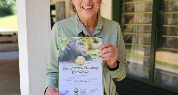 Un viajero sonriente muestra orgullosamente un certificado de rastreo de chimpancés fuera de un alojamiento.