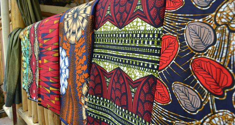 Telas africanas con patrones brillantes cuelgan en una fila en un exhibidor.