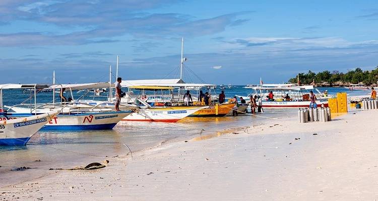Les bateaux à balancier s'alignent sur une plage de sable blanc sur l'île de Panglao tandis que les passagers et l'équipage se préparent pour la mer.