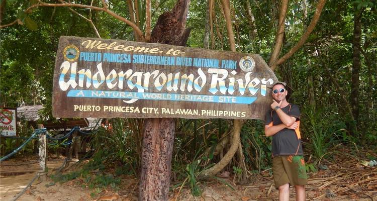 Voyageur posant à côté du panneau en bois coloré du Parc national de la Rivière souterraine de Puerto Princesa