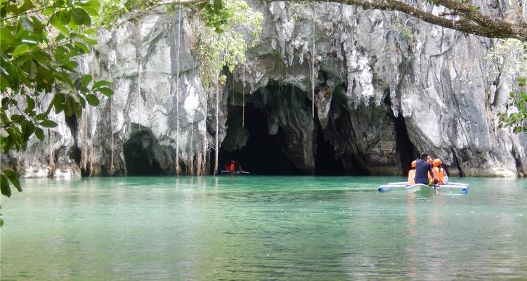 De petits bateaux à pagaie pénètrent dans l'imposante entrée calcaire de la Rivière Souterraine au-dessus d'une eau vert émeraude.