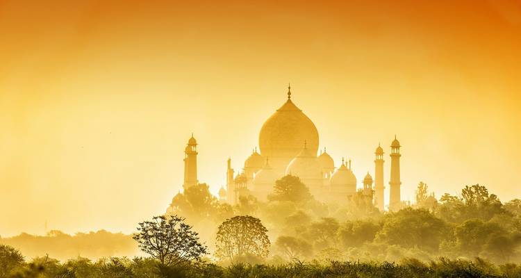 Une vue lointaine du Taj Mahal baigné d'une lumière dorée au lever ou au coucher du soleil.