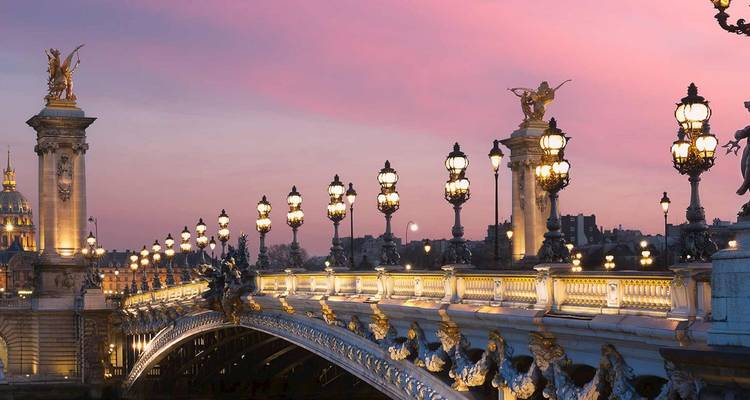El ornamentado puente Pont Alexandre III de París resplandece bajo un cielo crepuscular rosado, adornado con esculturas y lámparas doradas