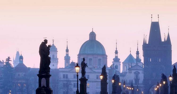 Estatuas silueteadas adornan el Puente de Carlos de Praga con cúpulas de iglesias y torres medievales que emergen a través de la niebla matutina.