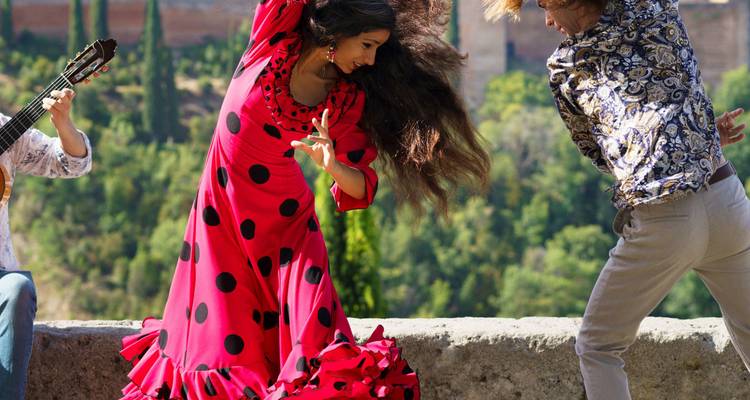 Bailarines de flamenco con trajes rojos brillantes y estampados actuando enérgicamente al aire libre con un guitarrista junto a ellos.