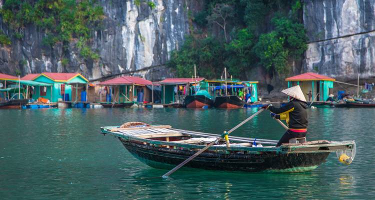 Woman paddling a traditional boat with a scenic backdrop of limestone cliffs.